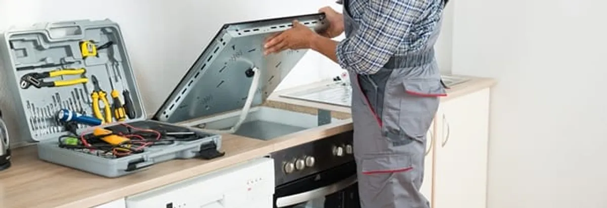 Cooktop repair technician lifting a built-in stovetop for service in Oakland, CA
