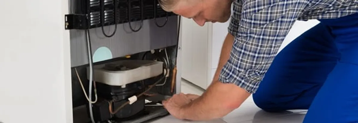 Refrigerator repair technician servicing the compressor and condenser area in Oakland, CA